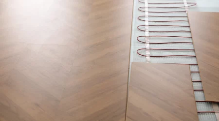 Installation von Laminatboden mit Fußbodenheizung: Detailaufnahme zeigt den Prozess der Verlegung von Laminatdielen über Heizkabeln, die auf einem Netz montiert sind.