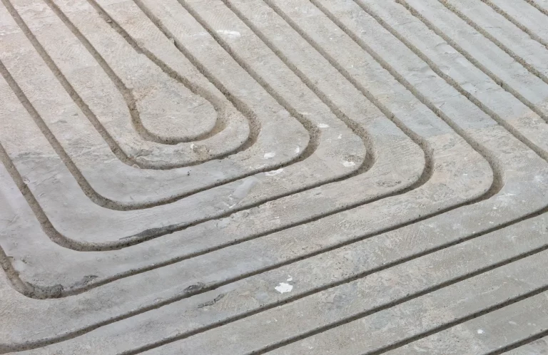 Detailaufnahme einer frisch gefrästen Estrichoberfläche mit präzisen, parallel verlaufenden Rillen, die zur Installation einer Fußbodenheizung vorbereitet wird.