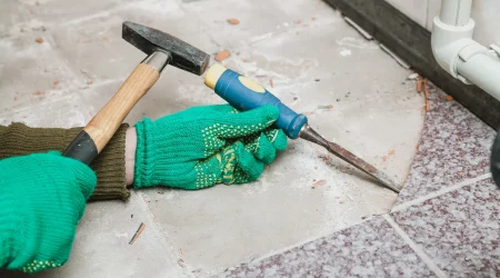 Ein Fliesenleger entfernt mit einem kleinen Meisel und einem Hammer verlegte Fliesen für die Vorbereitung einer Fußbodenheizung