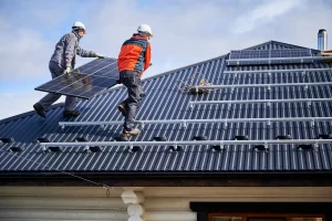 Zwei Handwerker in Arbeitskleidung installieren Photovoltaikmodule auf einem Hausdach.