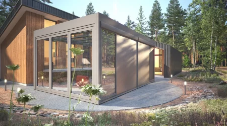 Modernes Haus mit einem Wintergartenanbau aus Glas, eingebettet in eine Waldlandschaft, mit natürlicher Vegetation im Vordergrund und Tageslicht, das den Raum erhellt.