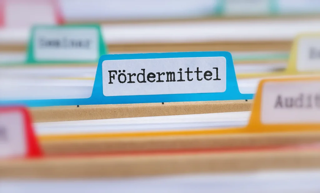 Nahaufnahme einer blauen Registerkarte in einem Aktenordner mit der Aufschrift 'Fördermittel', umgeben von anderen Registerkarten in verschiedenen Farben.