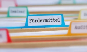 Nahaufnahme einer blauen Registerkarte in einem Aktenordner mit der Aufschrift 'Fördermittel', umgeben von anderen Registerkarten in verschiedenen Farben.