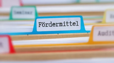 Nahaufnahme einer blauen Registerkarte in einem Aktenordner mit der Aufschrift 'Fördermittel', umgeben von anderen Registerkarten in verschiedenen Farben.
