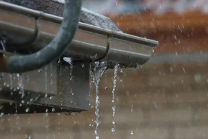 Eine undichte und rostige Dachrinne, aus der Wasser bei Regen herausfließt