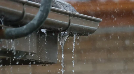 Eine undichte und rostige Dachrinne, aus der Wasser bei Regen herausfließt