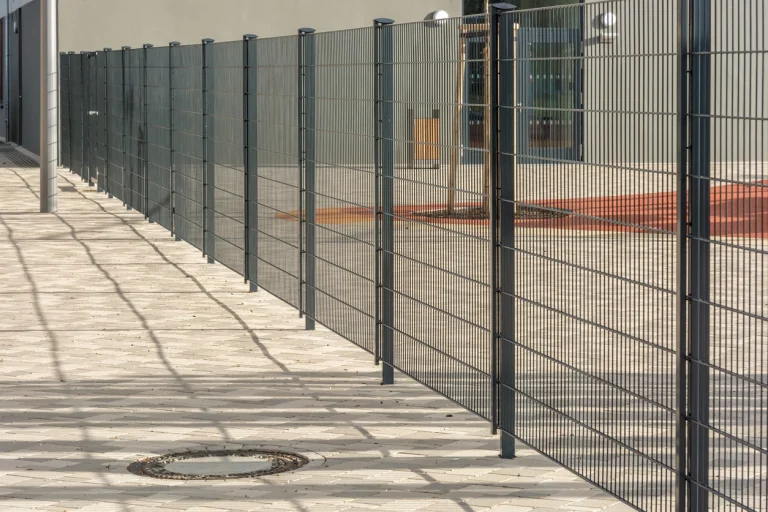 Zaun der ein Grundstück begrenzt und schatten auf das Pflaster wirft