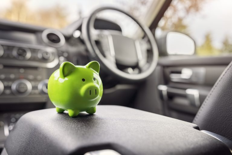 grünes Sparschwein steht im Inneren eines Autos.
