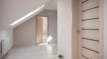 Heller Raum mit zwei modernen Innentüren aus Holz. Die vordere Tür hat horizontale Glasstreifen, während die hintere Tür offen steht und in ein weiteres Zimmer führt. Die Türen sind aus hellem Holz gefertigt und fügen sich in das minimalistische Design des Raumes ein.