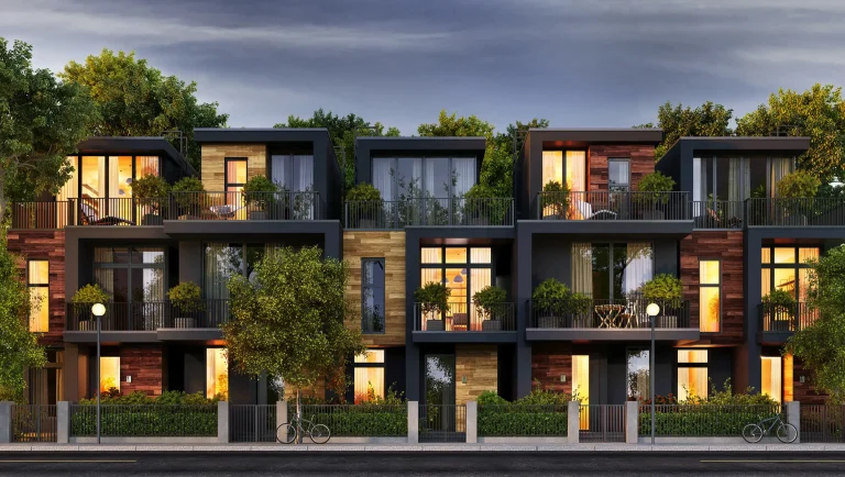 Moderne Reihenhäuser mit großen Glasfenstern und Balkonen, umgeben von Bäumen und Grünflächen. Die moderne Fassadengestaltung kombiniert dunkle Akzente mit Holzverkleidungen und minimalistischen Designelementen. Außenbeleuchtung und Vegetation schaffen eine einladende Atmosphäre in einem urbanen Wohnviertel.