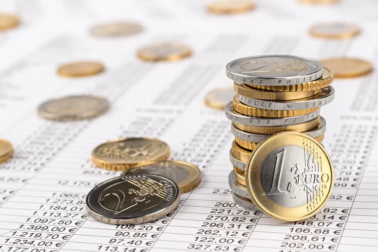 Gestapelte Euro-Münzen auf einem Finanzdokument mit Zahlenreihen, symbolisieren Finanzen, Buchhaltung oder Kostenrechnung.