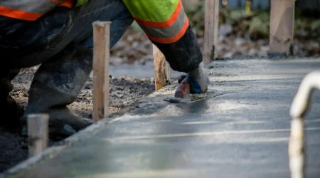 Handwerker in reflektierender Arbeitskleidung glättet mit einer Kelle frisch gegossenen Beton für das Fundament eines Wintergartens.