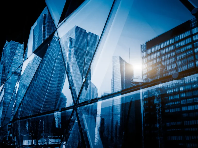 Spiegelung moderner Wolkenkratzer in einer Fassade aus Glas, mit blauer Farbgebung und geometrischen Formen