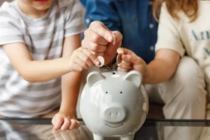 Eine Familie steckt jeweils ein Geldstück in ein weißes Sparschwein