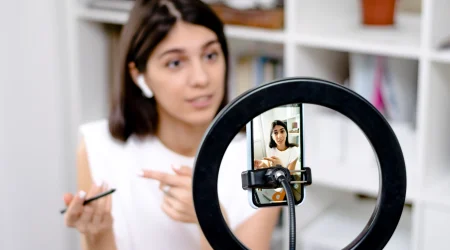Influencerin sitzt vor ihrem Ringlicht und Handy und nimmt Content für ihre Follower auf