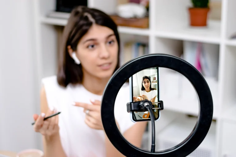 Influencerin sitzt vor ihrem Ringlicht und Handy und nimmt Content für ihre Follower auf