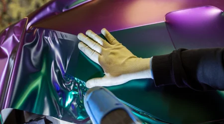 Mensch foliert Auto mit metallischer Folie und einem Heißluftföhn