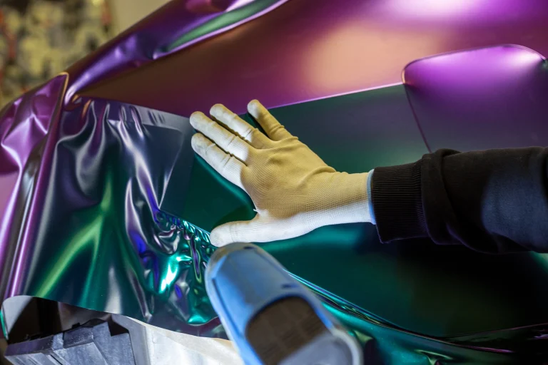 Mensch foliert Auto mit metallischer Folie und einem Heißluftföhn