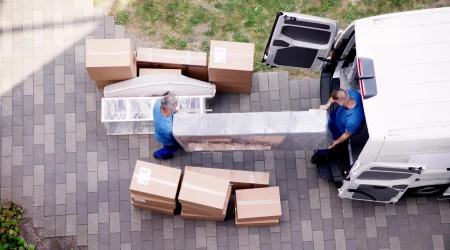 Zwei Möbelpacker heben ein großes verpacktes Möbelstück in einen weißen Transporter.