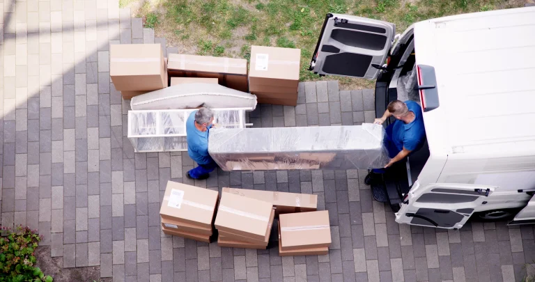 Zwei Möbelpacker heben ein großes verpacktes Möbelstück in einen weißen Transporter.