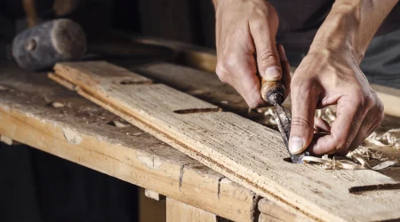 Hände die ein Stück Holz bearbeiten