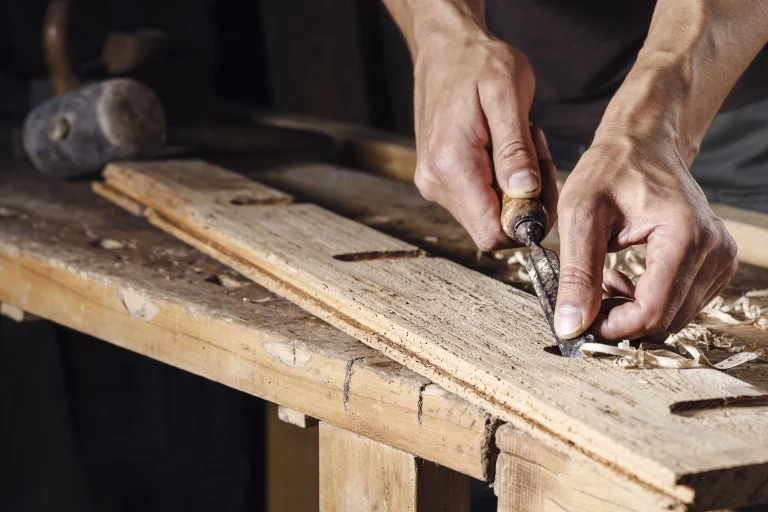 Hände die ein Stück Holz bearbeiten