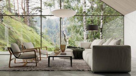 Alt-Text: Moderner Wohnbereich mit bodentiefen Glaswänden, die einen Panoramablick auf eine grüne Waldlandschaft bieten. Der Raum ist mit einer grauen Couch, zwei eleganten Sesseln aus Holz, einem flauschigen Teppich und einem minimalistischen Couchtisch ausgestattet. Eine Hängelampe und ein Stehlampen-Design ergänzen das stilvolle Ambiente.