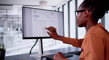 Frau analysiert digitale Rechnung auf großem Monitor in modernem Büro.