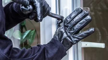 Einbrecher mit schwarzen Lederhandschuhen versucht ein Fenster aufzuhebeln.