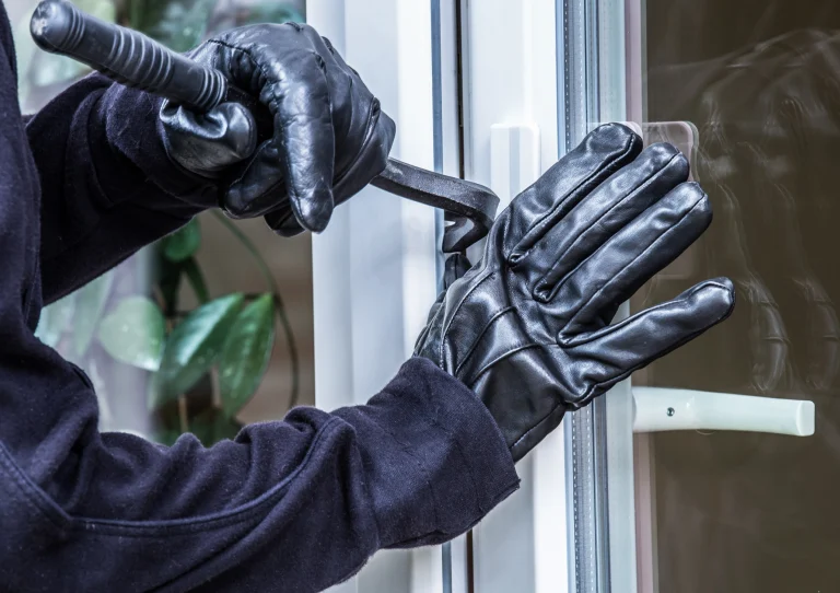 Einbrecher mit schwarzen Lederhandschuhen versucht ein Fenster aufzuhebeln.