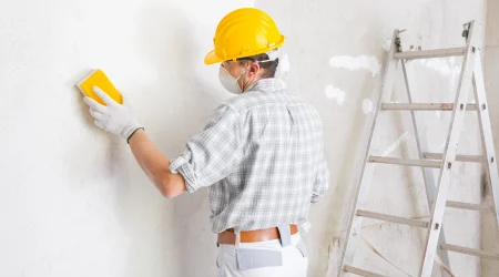 Trockenbaumonteur begradigt durch abschleifen der Oberfläche die verputzte Wand.