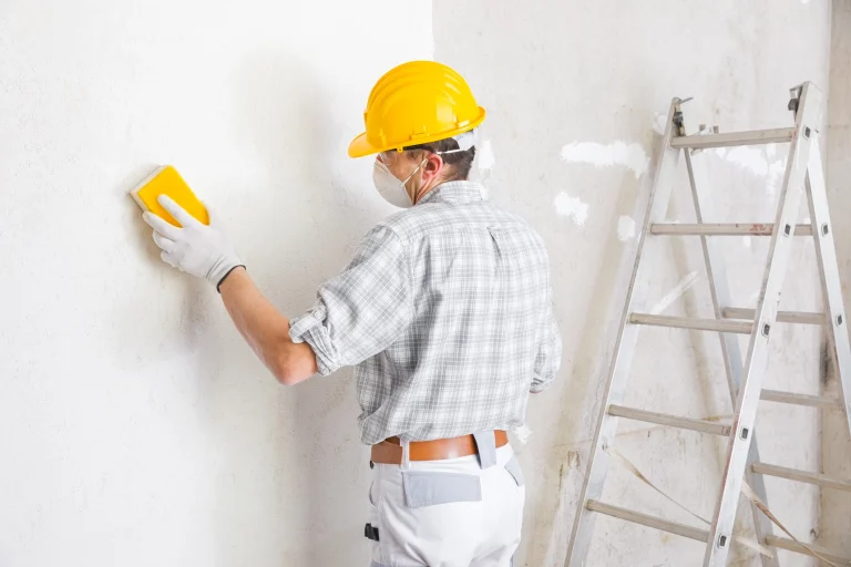 Trockenbaumonteur begradigt durch abschleifen der Oberfläche die verputzte Wand.