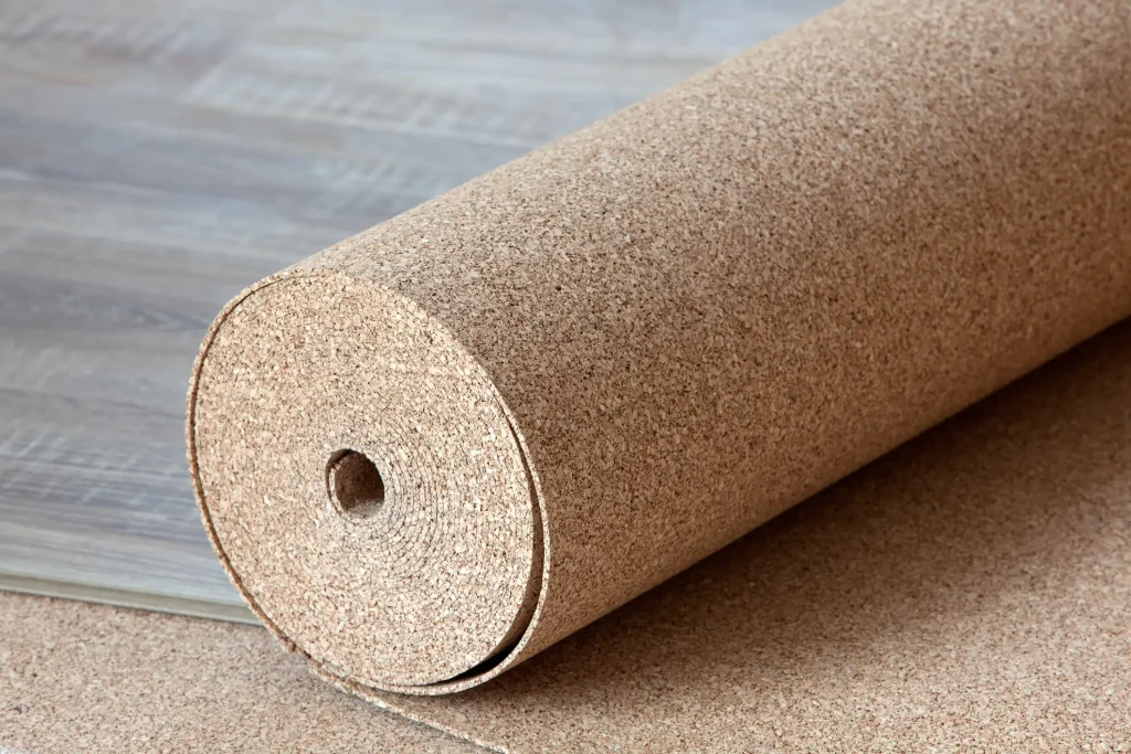 Große Rolle aus Korkmaterial, teilweise ausgerollt auf einem Holzboden. Der Kork hat eine feine, körnige Struktur und wird als Bodenunterlage genutzt. Im Hintergrund sind Holzpaneele sichtbar.