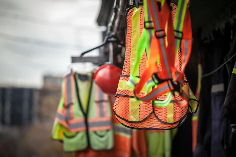 Neonfarbene Arbeitsjacken hängen auf einer Baustelle.