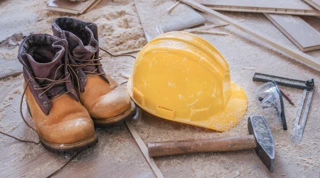 Sicherheitsschuhe und ein Sicherheitshelm liegen auf dem Boden einer Baustelle.