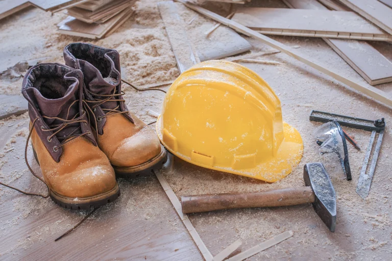 Sicherheitsschuhe und ein Sicherheitshelm liegen auf dem Boden einer Baustelle.