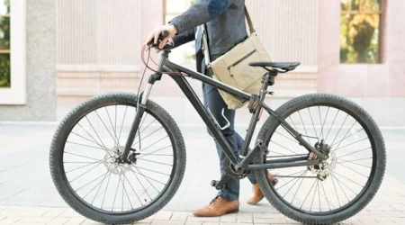 Ein Mann in grauem Anzug und mit einer Aktentasche um die Schultern, steigt auf ein dunkles Fahrrad auf.