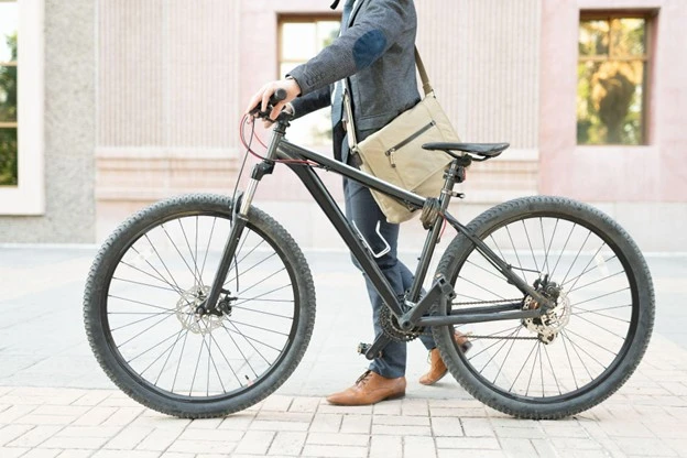 Ein Mann in grauem Anzug und mit einer Aktentasche um die Schultern, steigt auf ein dunkles Fahrrad auf.