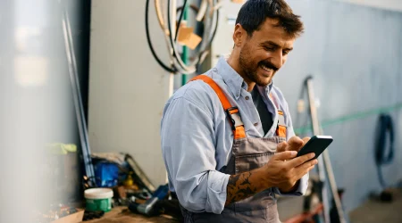Handwerker tippt auf seinem Handy, um eine seine App zu öffnen.