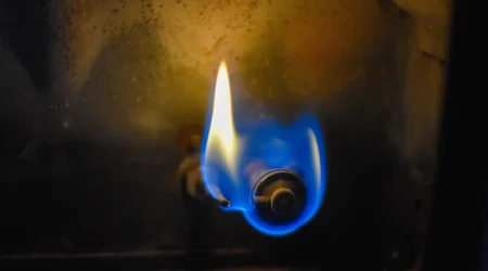 Nahaufnahme des Brenners einer Gasheizung mit einer blauen und gelben Flamme.