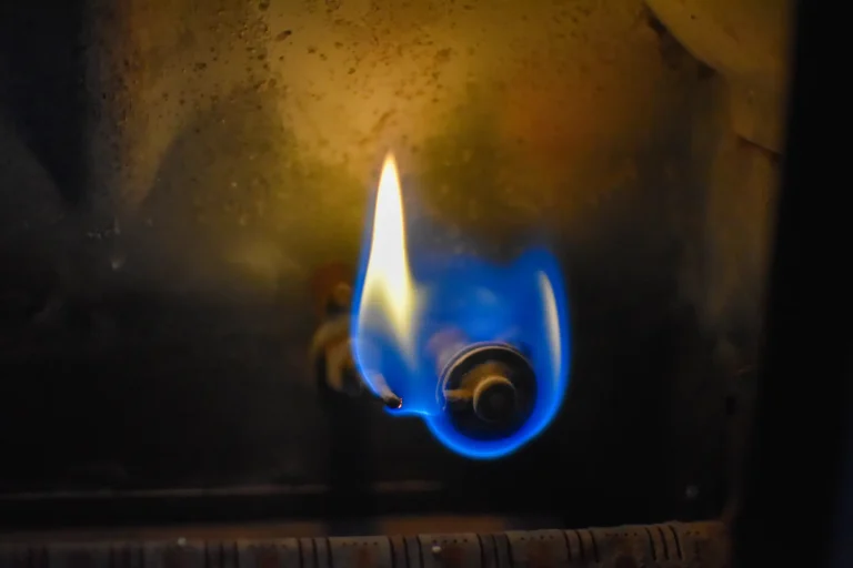 Nahaufnahme des Brenners einer Gasheizung mit einer blauen und gelben Flamme.