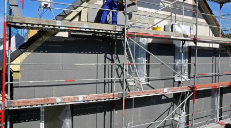 Fassadenarbeiten an einem Einfamilienhaus mit Baugerüst: Fassadenbauer bringt Fassadendämmplatten an, während die Fassade für die weitere Gestaltung vorbereitet wird.