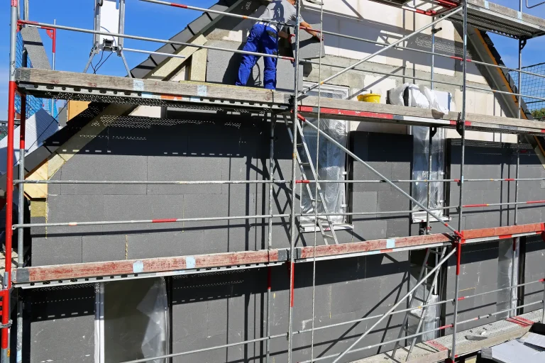 Fassadenarbeiten an einem Einfamilienhaus mit Baugerüst: Fassadenbauer bringt Fassadendämmplatten an, während die Fassade für die weitere Gestaltung vorbereitet wird.