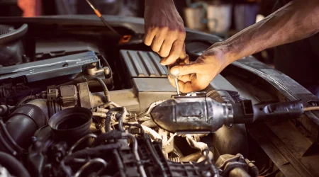Nahaufnahmen von Händen im Motorraum eines Autos, die darin etwas abschrauben.