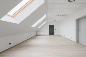 Modern ausgebautes Dachgeschoss mit tapezierten Schrägen und Kniestock, Tageslichteinfall durch Dachfenster und hellem Bodenbelag.