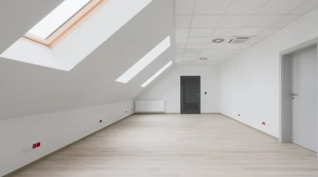 Modern ausgebautes Dachgeschoss mit tapezierten Schrägen und Kniestock, Tageslichteinfall durch Dachfenster und hellem Bodenbelag.