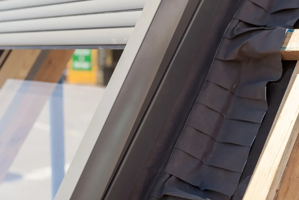 Nahaufnahme eines seitlichen Fensterrahmens eines Dachfensters mit deutlich sichtbarer Wärmedämmung und Schwammdichtungen zur Isolierung von außen.