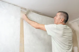 Handwerker tapeziert eine Wand und passt eine Tapetenbahn sorgfältig in eine Raumecke ein – ein typischer Arbeitsschritt beim exakten Tapezieren von Innenraumecken.