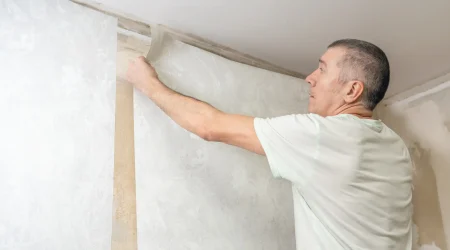 Handwerker tapeziert eine Wand und passt eine Tapetenbahn sorgfältig in eine Raumecke ein – ein typischer Arbeitsschritt beim exakten Tapezieren von Innenraumecken.