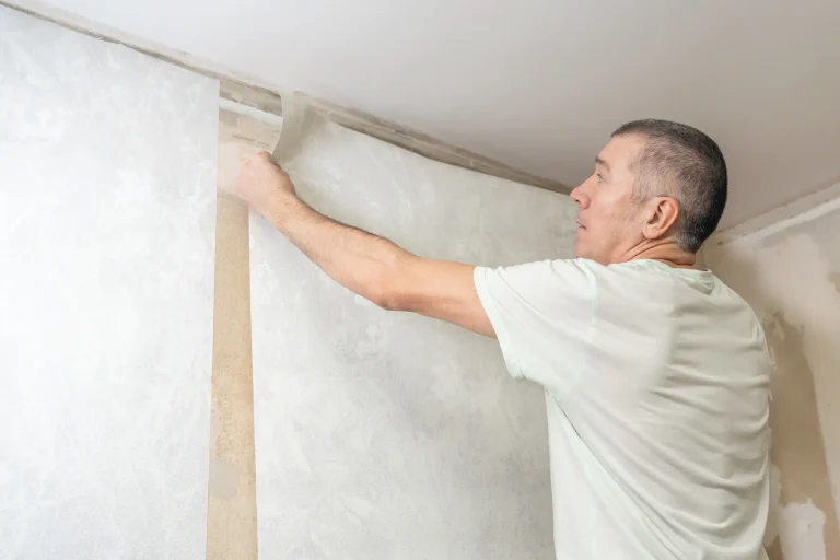 Handwerker tapeziert eine Wand und passt eine Tapetenbahn sorgfältig in eine Raumecke ein – ein typischer Arbeitsschritt beim exakten Tapezieren von Innenraumecken.
